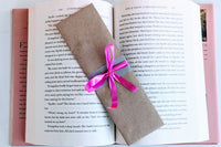 A Romance-themed bookmark is wrapped in brown craft paper and decorated with pink ribbon. It rests on an open hardback book.