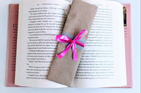 A Romance-themed bookmark is wrapped in brown craft paper and decorated with pink ribbon. It rests on an open hardback book.