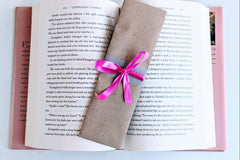 A Romance-themed bookmark is wrapped in brown craft paper and decorated with pink ribbon. It rests on an open hardback book.