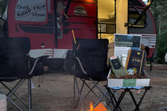 A picture of that road trip mom's escape and explore subscription box in front of a red camper at a campsite .