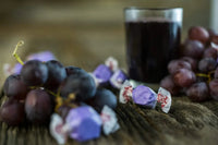 Fresh squeezed red grape juice with purple grape saltwater taffy sitting on a wooden table. With grapes on a vine scattered around. 