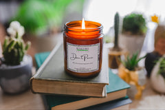 a jarred candle sits atop a stack of old books. Succulents and other plants are blurred in the background.