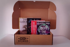 Brown box filled with an assortment of books from various genres, including mystery, romance, and fantasy, featuring vibrant covers.