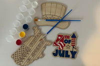 Three wooden patriotic shapes with 2 paint brushes and a paint sampler. One of the shapes is painted as an example.