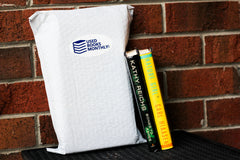 A stack of used books in front of a Used Books Monthly subscription box showcasing a book subscription service