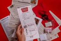 Scarlet Envelope Secret Society subscription box with red envelope, mystery clues, and a glass of wine for a date night experience