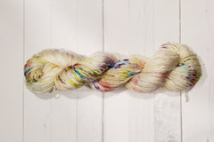 A Skein of Hand Dyed Silk Yarn in Worsted Weight with various colors speckled throughout on a cream base