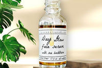 The Day Glow Face Serum by Greenmade goods sitting on a wooden podium with monstera plants in the background.