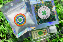 Components of the Leprechaun Slime Kit including jello, glitter, and clay. Clear glue in a foil pouch with sticker labels.
