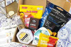 An open Sleek Treat subscription box filled with snacks, including chocolate cups, gummies, cheese crisps and a granola bar.