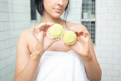 brunette woman wrapped in a white bath towel holding up two lime green shower steamers in a bathroom with white tile
