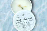 Jas Hands Hand Salve by Greenmade goods. An open tin showing the salve with jasmine buds on top and sitting in a pool of shimmering water.