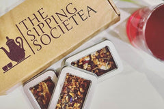 The Sipping Societea Loose leaf tea subscription box with tea tins and next to raspberry lemonade iced tea.