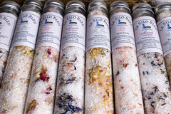 Severall tubes of bath salts detailing botanicals in various colors for each scent laying on a table all lined up together.