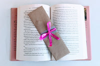 A Romance-themed bookmark is wrapped in brown craft paper and decorated with pink ribbon. It rests on an open hardback book.