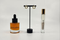 LOKA.HAUS beauty: 'Duality Oil' in amber, center 'Intensity Parfum Roller', & luxe gold earrings on right. Elegance in a subscription box