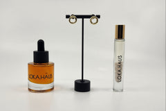 LOKA.HAUS beauty: 'Duality Oil' in amber, center 'Intensity Parfum Roller', & luxe gold earrings on right. Elegance in a subscription box
