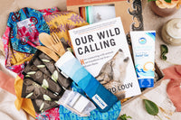 An open Seasonal Earthlove subscription box filled with a novel, bamboo cooking utensils, sunburn relief gel and more.