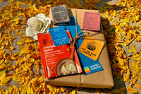 Book wrapped in brown paper and twine laying in orange leaves. Book-themed goodies lay next to and on top of the book