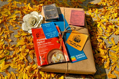 Book wrapped in brown paper and twine laying in orange leaves. Book-themed goodies lay next to and on top of the book