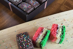 Nettie's Craft Brownies rainbow cookies sprinkles chocolate dipped angled view of cookies on cutting board.