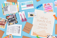 Music-themed box with earrings, art print "when words fail, music speaks" , concert ticket greeting card, and stereo pin on blue background.
