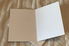 An open card showing that the inside of the card is blank.  Open card laying on top of an envelope on top of an off white fuzzy background.