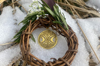 A small wreath made of twigs adorned with rosemary and a gold Tree of Life pendant from the Busy Witch Box subscription box