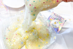 Chick-a-dee-do=dah slime kit prepared and oozing out of someone's hand into the container. Pale yellow with clay chickens and easter eggs.