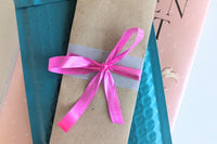 A Romance-themed bookmark is wrapped in brown craft paper and decorated with pink ribbon. It rests on an open hardback book.