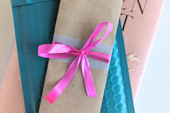A Romance-themed bookmark is wrapped in brown craft paper and decorated with pink ribbon. It rests on an open hardback book.