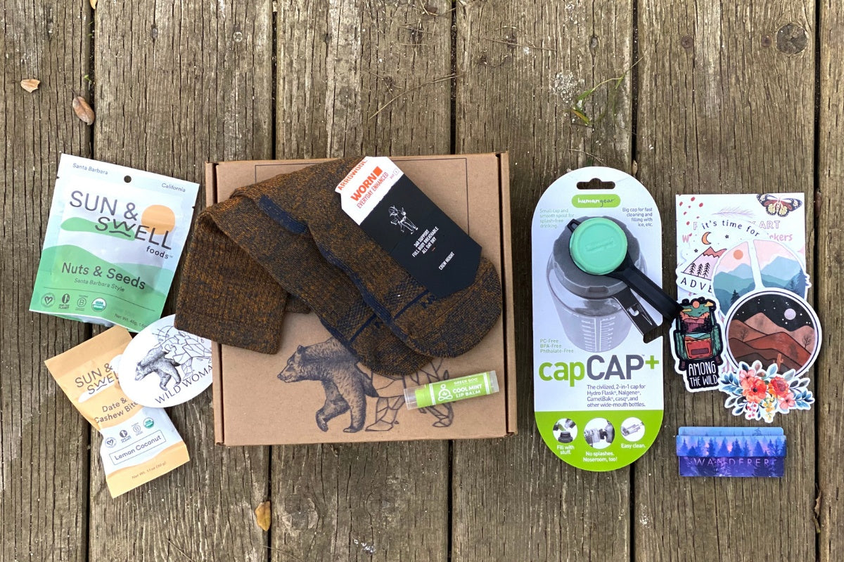 Wild Woman Box subscription boxes stacked on a mountain ledge with a scenic view in the background