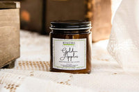 a jarred candle named golden apples sits on top of a white lace tablecloth. a brown wooden box sits to the left of the candle.
