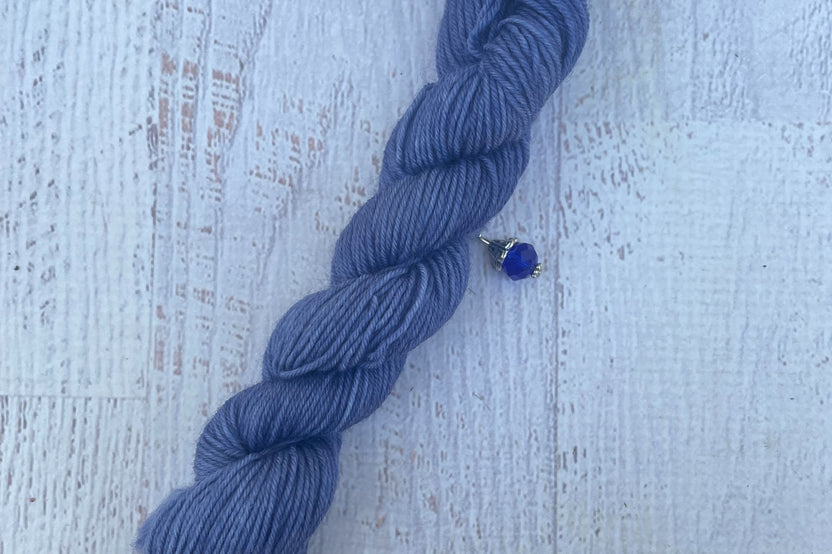 A mini Skein of Hand Dyed Merino Sock Weight Yarn and a coordinating stitch marker. Suitable for knitting and crocheting 
