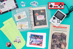 An 80s themed box with a sticker album, game boy, and greeting card among other gifts on a blue background. 