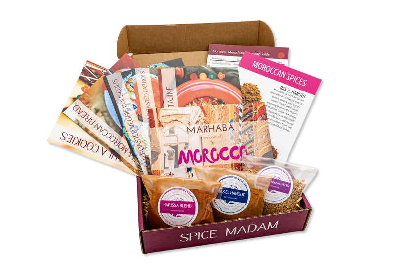 An open food subscription box labeled Spice Madam that is filled with 3 bags of spices and lots of recipe cards.