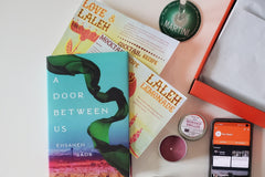 Items from a The Chaptr subscription box including a book, a small candle in a tin, and cocktail recipes.