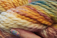 A close up of a Skein of Hand Dyed Baby Alpaca Chunky Weight Yarn in a mix of gold, yellow, blue and green 