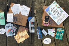 Wild Woman Box subscription boxes stacked on a mountain ledge with a scenic view in the background