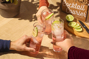 Image of three hands saying cheers with three tall pink cocktails garnished with fresh lime circles. 