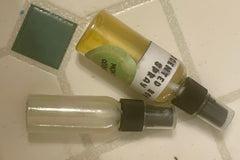 Two small spray bottles lie next to each other against some tiles. The bottle's label reads, "scented body spray."