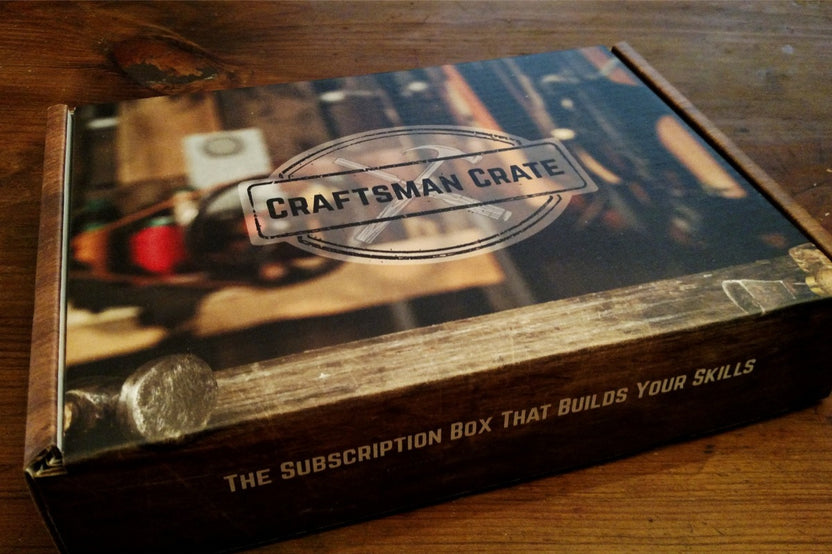 A subscription box labeled Craftsman Crate sitting on a wooden table. The box has an image of a workshop on the front.