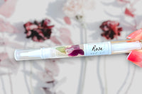 Hand Holding The Rose Botanical Nail Pen by Greenmade goods with flowers and shadows in the Background.