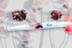 Hand Holding The Rose Botanical Nail Pen by Greenmade goods with flowers and shadows in the Background.