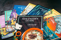 An assortment of Stranger's Guides. They include Vietnam, Lagos, Ireland, South Korea, Tehran, Scandinavia, Texas, and California.