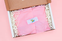 The Oddball Club subscription box opened with pink tissue paper, crinkle box filler, and a sticker holding the tissue paper closed.