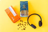 This photo contains bags of coffee and headphones along. Also contains several  coffee beans randomly arranged.