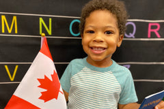 A child hold up a Canadian flag and passport that is included in the Wiggle Worms Around the World kit-Canada. 