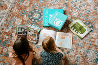 Two children reading books from Bookroo's Tween Book Club subscription on a colorful rug with additional books nearby