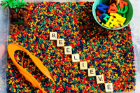 Chicka Chicka Boom Inspired Sensory Bin with primary color dyed alphabet pasta, scrabble letters, rubber letters palm tree and pom poms